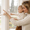 Weißer Fenstergriff an Fenster angebracht und Frau mit Baby schaut aus Fenster